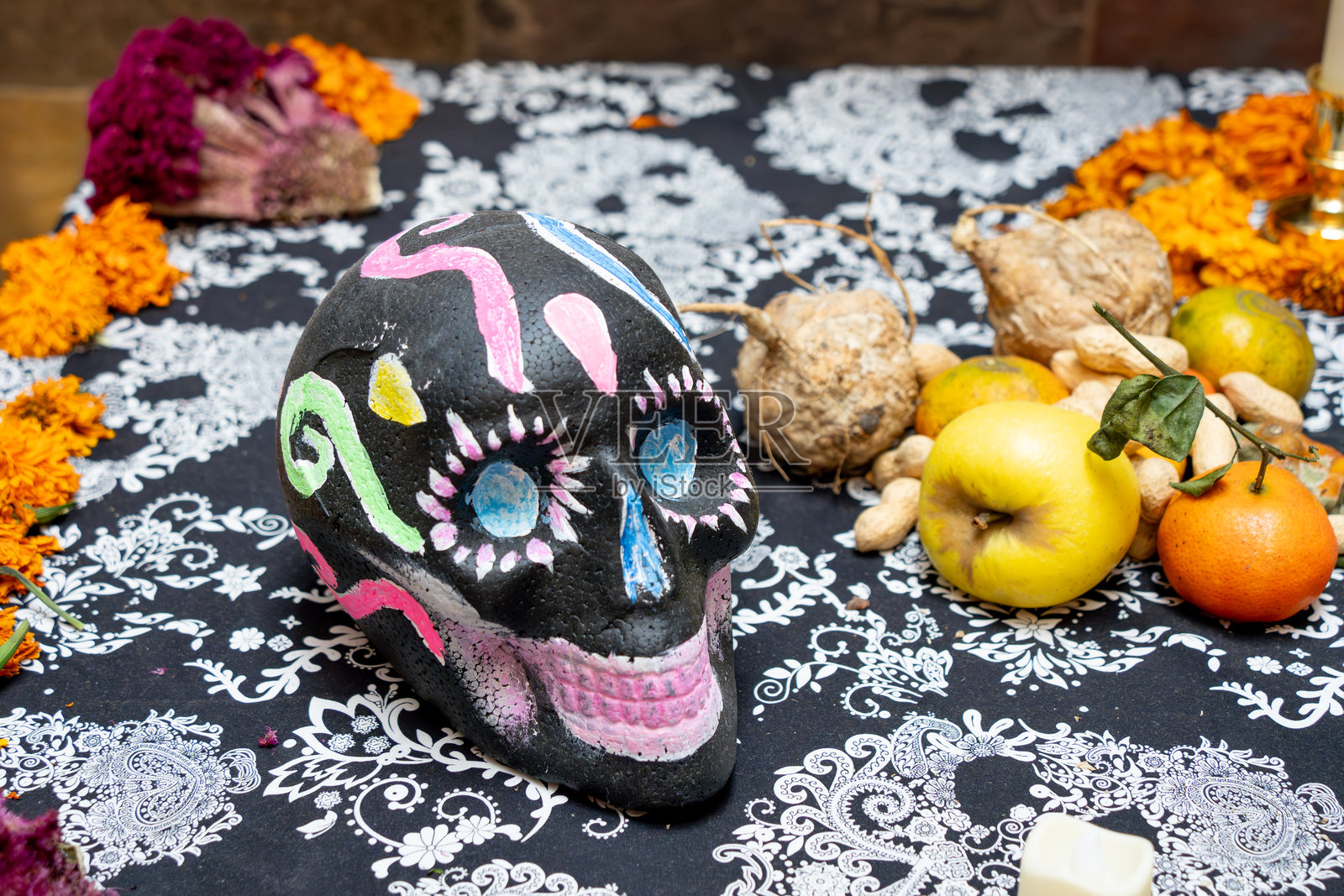 一具涂有彩色油漆的骷髅放在桌子上，旁边有水果和花朵。这是墨西哥的亡灵节庆祝活动，包含了剪纸工艺、供品和卡特里娜女士。照片摄影图片