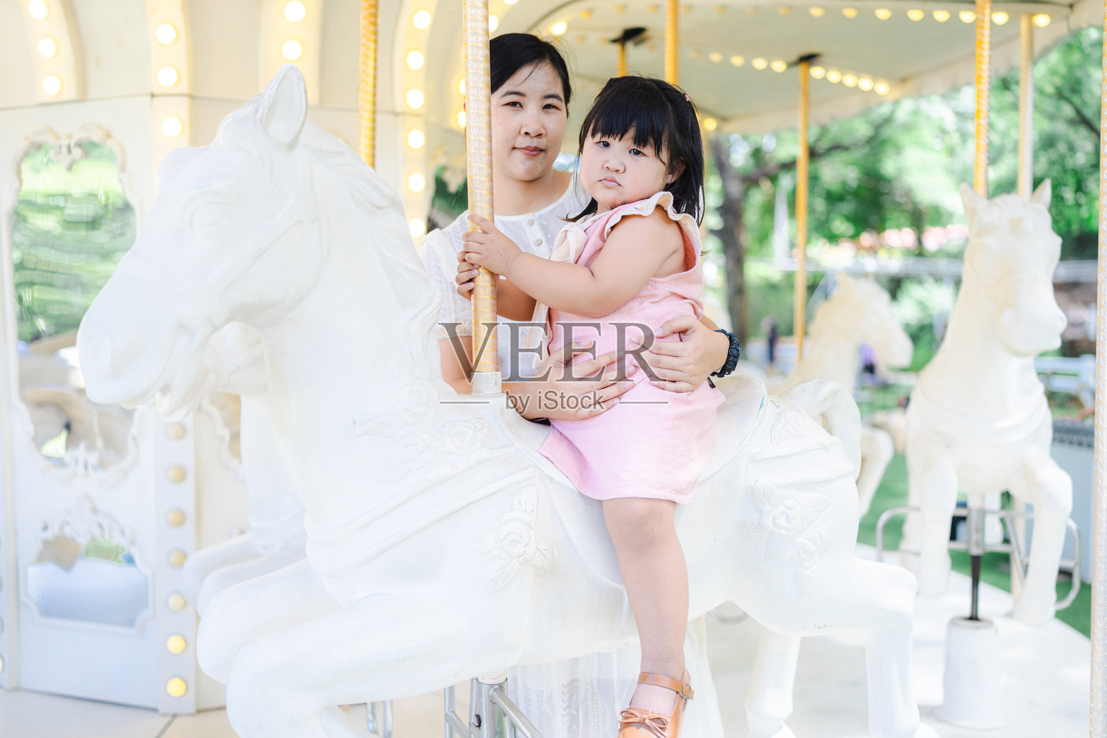 一位可爱的亚洲母亲和女儿在游乐园快乐地骑旋转木马，幸福的家庭，迷人的女性和可爱的小女孩在假期旅行时感到快乐和放松。照片摄影图片