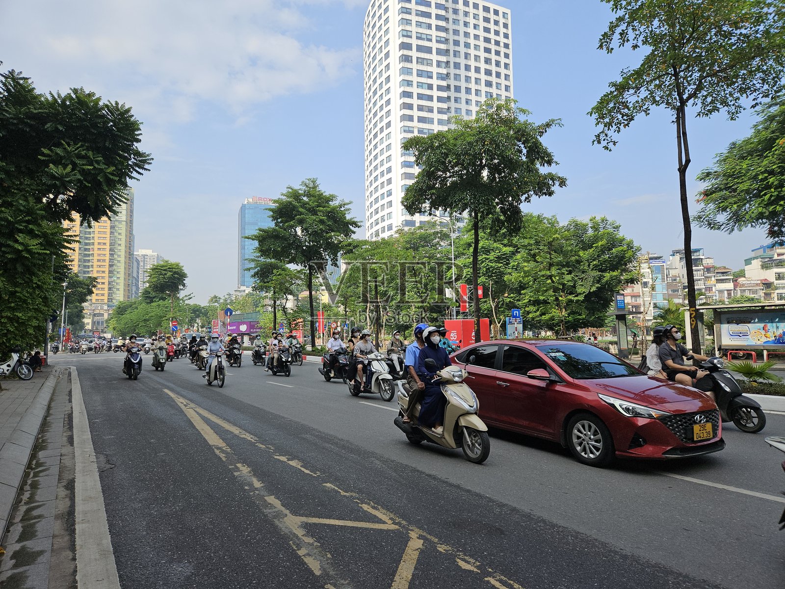 一条繁忙的宽街，满是摩托车和汽车，现代高楼大厦和郁郁葱葱的树木沿街而立。照片摄影图片