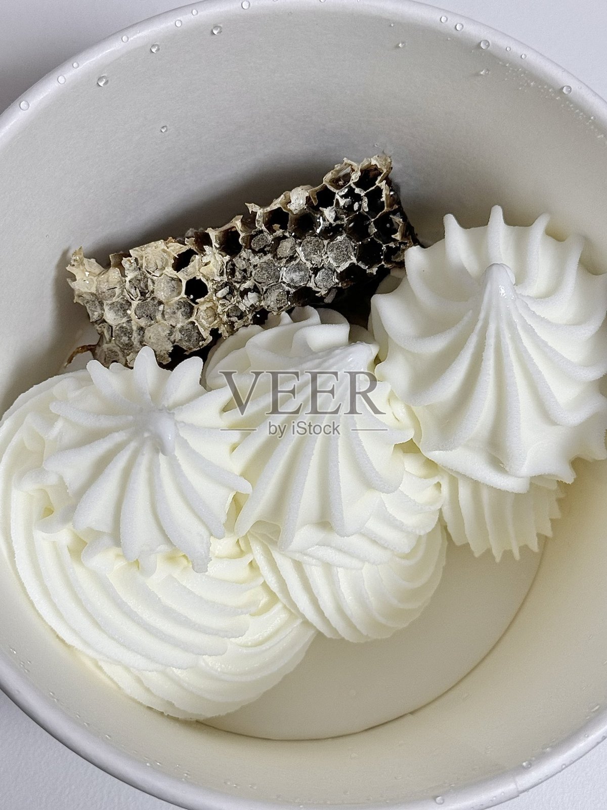 漩涡状酸奶冰淇淋甜点盛在杯子里，光滑细腻的质地和光泽的表面，上面点缀着新鲜水果块，突显出其清新诱人的外观。照片摄影图片