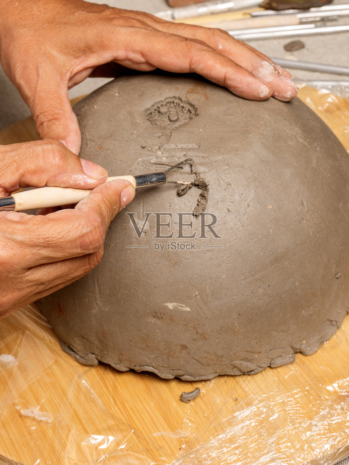 人手用陶艺工具塑形和雕刻粘土。工作坊中的陶瓷制作过程。照片摄影图片