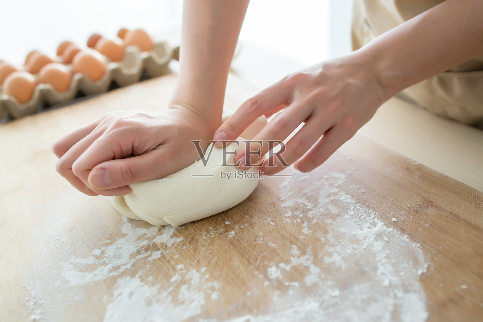 在木质表面上揉面团的人，背景中有鸡蛋。照片摄影图片