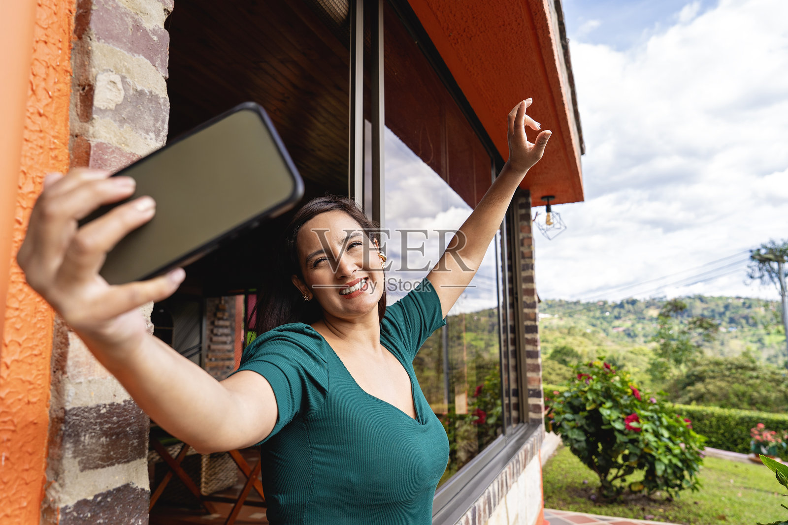 女人在窗边户外用智能手机自拍。照片摄影图片