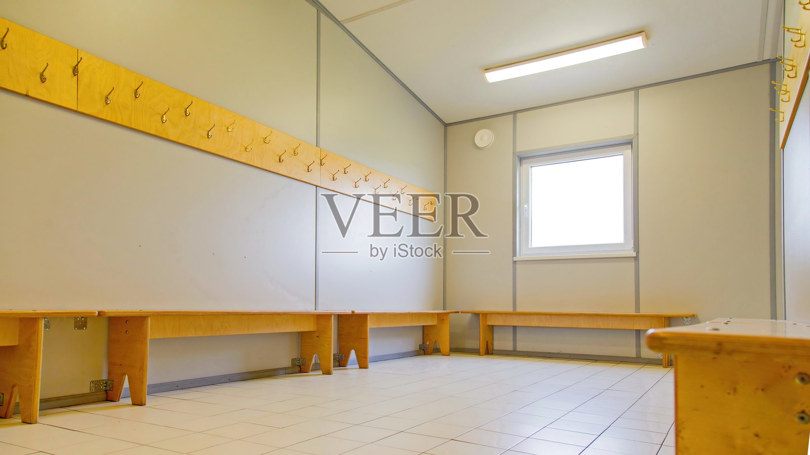 空荡荡的更衣室，墙上有木制长椅和衣帽钩。明亮的室内，铺有瓷砖地板，只有一扇窗户。照片摄影图片