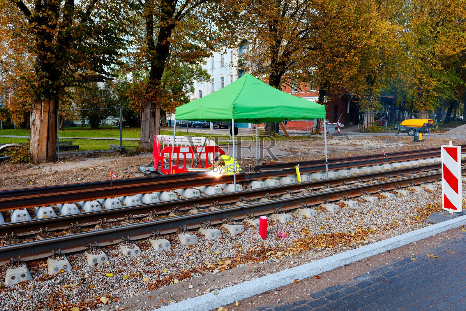 铁路工人在施工现场的绿色帐篷下焊接轨道进行维护。安全屏障和防护设备确保安全的工作环境。照片摄影图片