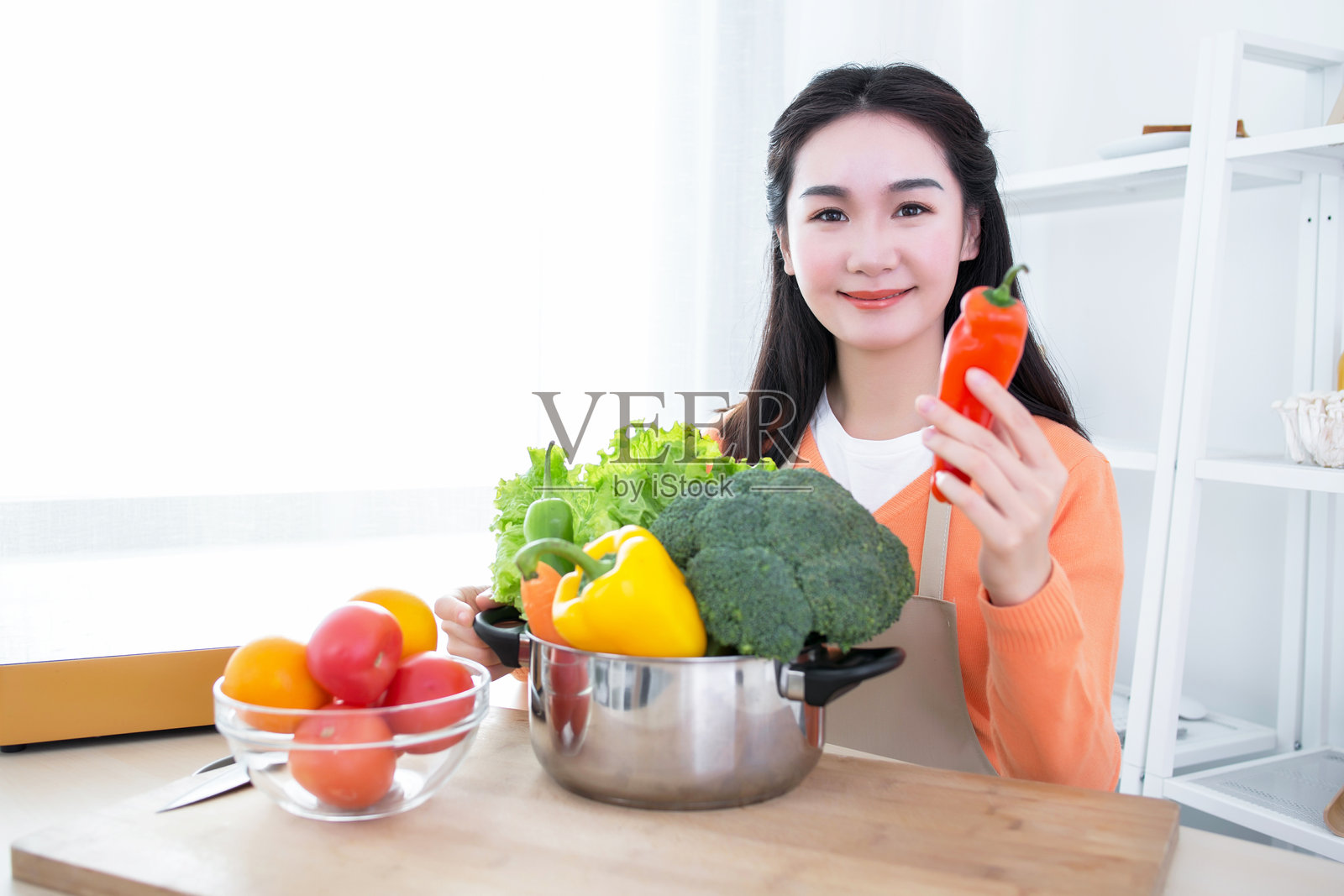 女人手持红辣椒，桌上摆放着各种蔬菜照片摄影图片