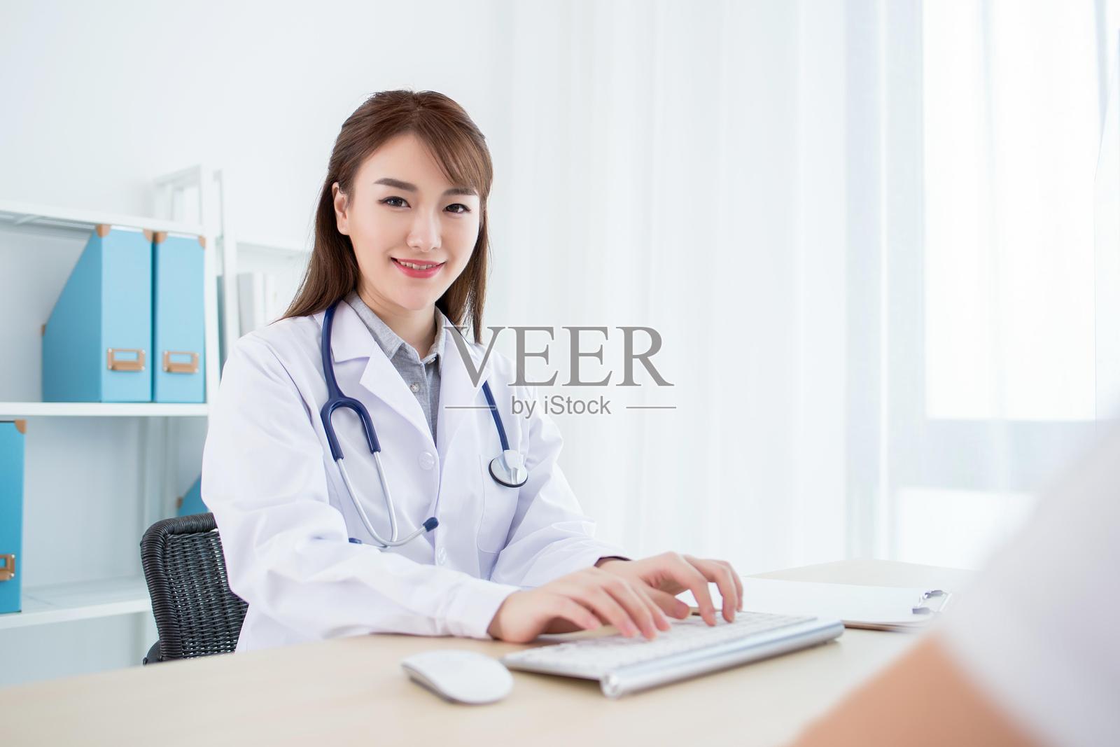 穿着白大褂的女医生在桌子上使用电脑工作照片摄影图片