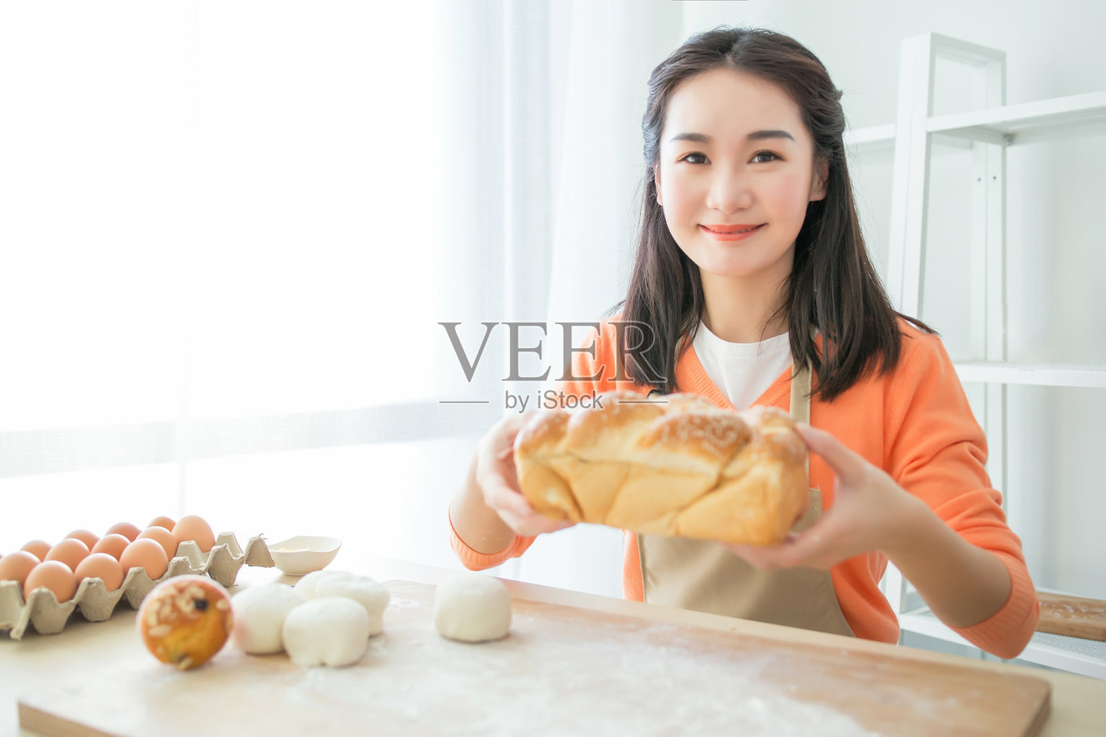 年轻女性在明亮的厨房里拿着新鲜出炉的面包照片摄影图片