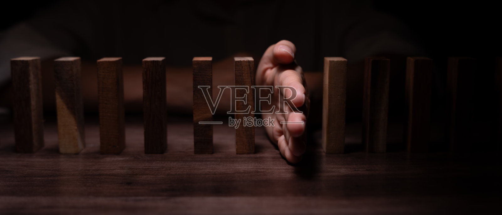 保险与手保护多米诺骨牌。商人用手阻止多米诺骨牌在商业危机中倒下。商业风险控制、规划和策略以防止保险业务的损失。照片摄影图片