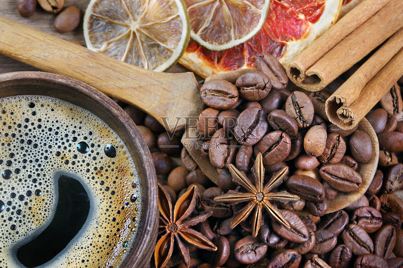 木勺中的烘焙咖啡豆和八角，木桌上的肉桂和干柑橘。泡沫咖啡杯、咖啡豆和香料。俯视图。照片摄影图片
