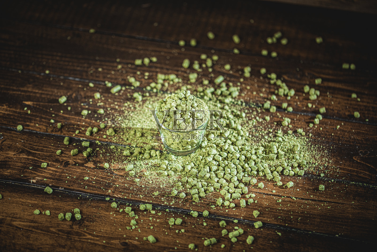 绿色水晶散落在木质表面上，旁边有一个小玻璃杯装着更多的这种物质。照片摄影图片