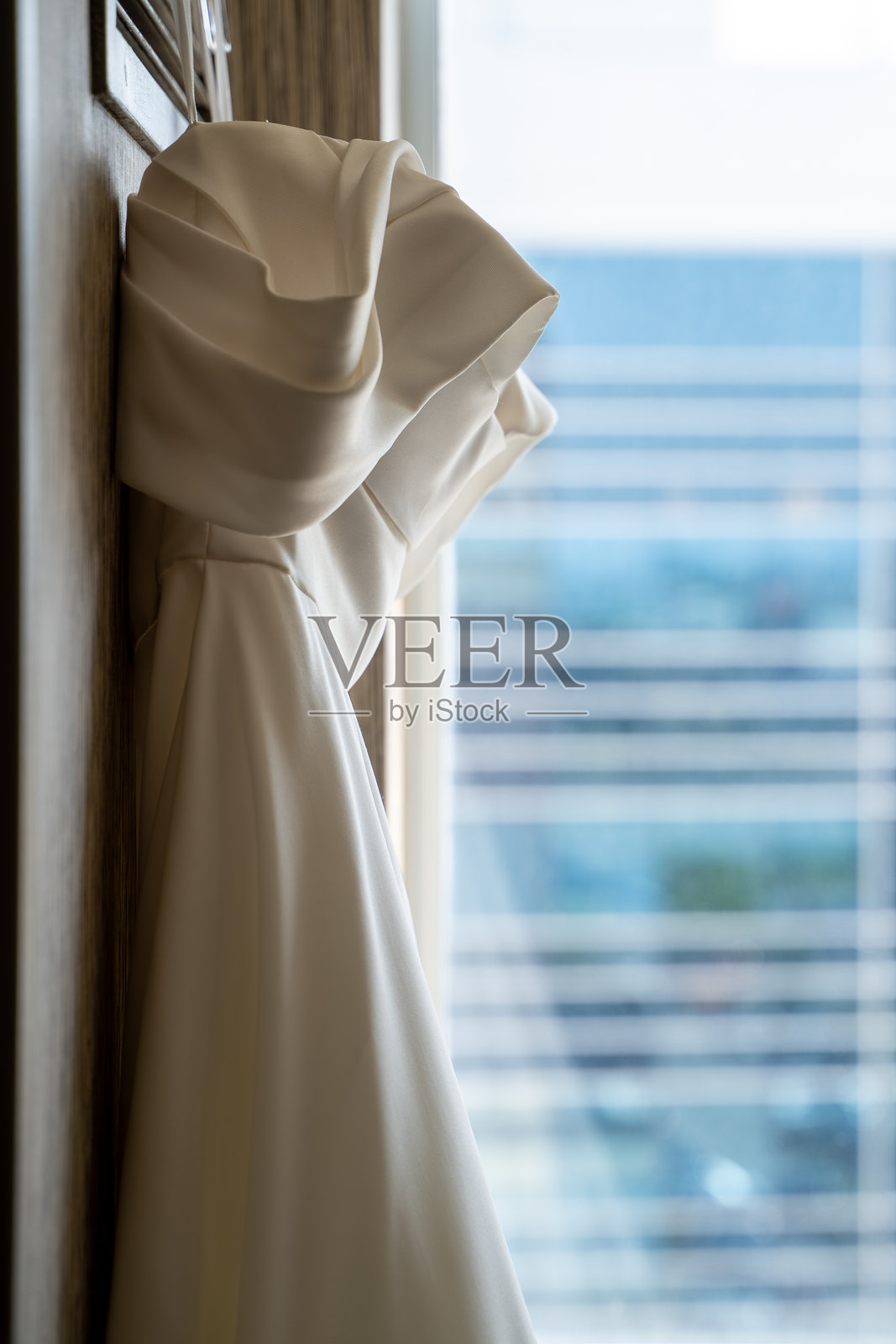 优雅的白色婚纱近距离挂在窗边。照片摄影图片