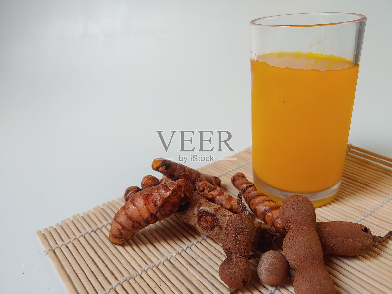 姜黄酸饮，传统草本饮料，由姜黄和罗望子制成，盛在透明玻璃杯中，背景为白色。照片摄影图片