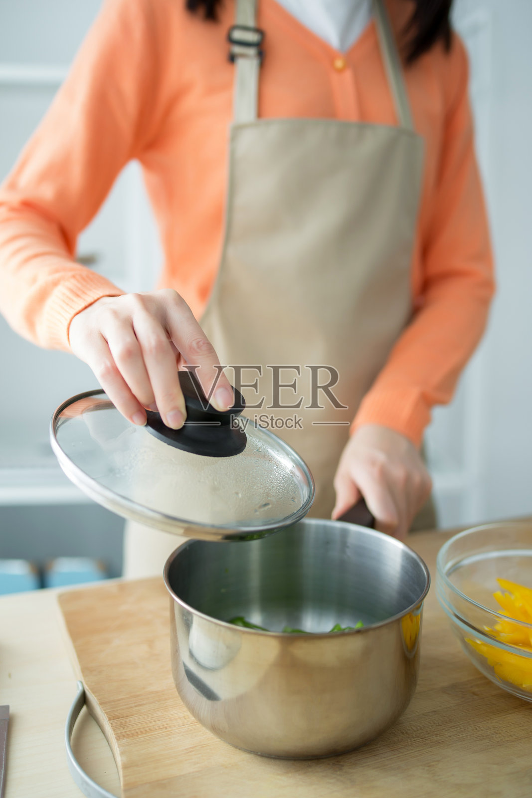 穿着围裙的女人在厨房里打开锅盖烹饪照片摄影图片