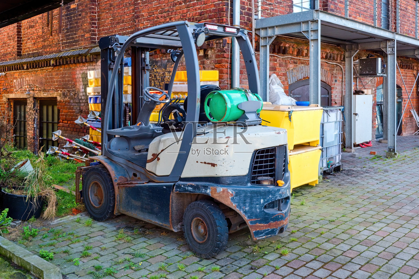 停放在砖砌建筑附近的工业院子里的旧叉车，配有气瓶。用于货物处理和运输的工业设备和机械。照片摄影图片