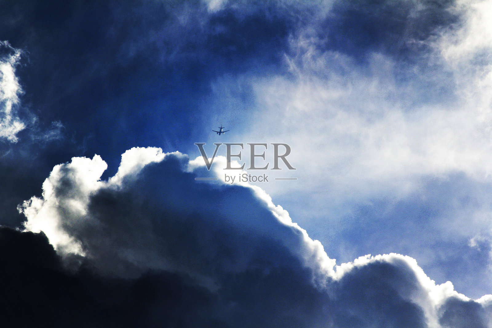 一架飞机在明亮的蓝天中翱翔，周围是蓬松的白云。照片摄影图片