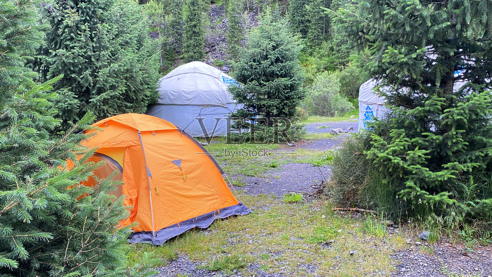 靠近科尔赛湖的露营地。一次前往哈萨克斯坦的旅行。一顶橙色的旅游帐篷矗立在绿色森林中的哈萨克民族毡房旁。照片摄影图片