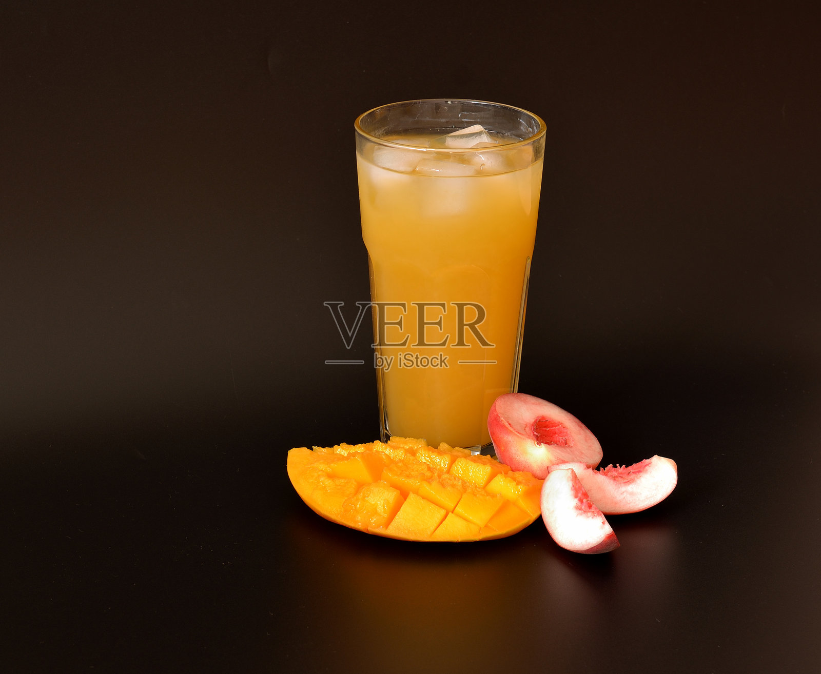 黑色背景上的果汁杯，杯中放有冰块，旁边有成熟的芒果和桃子。照片摄影图片