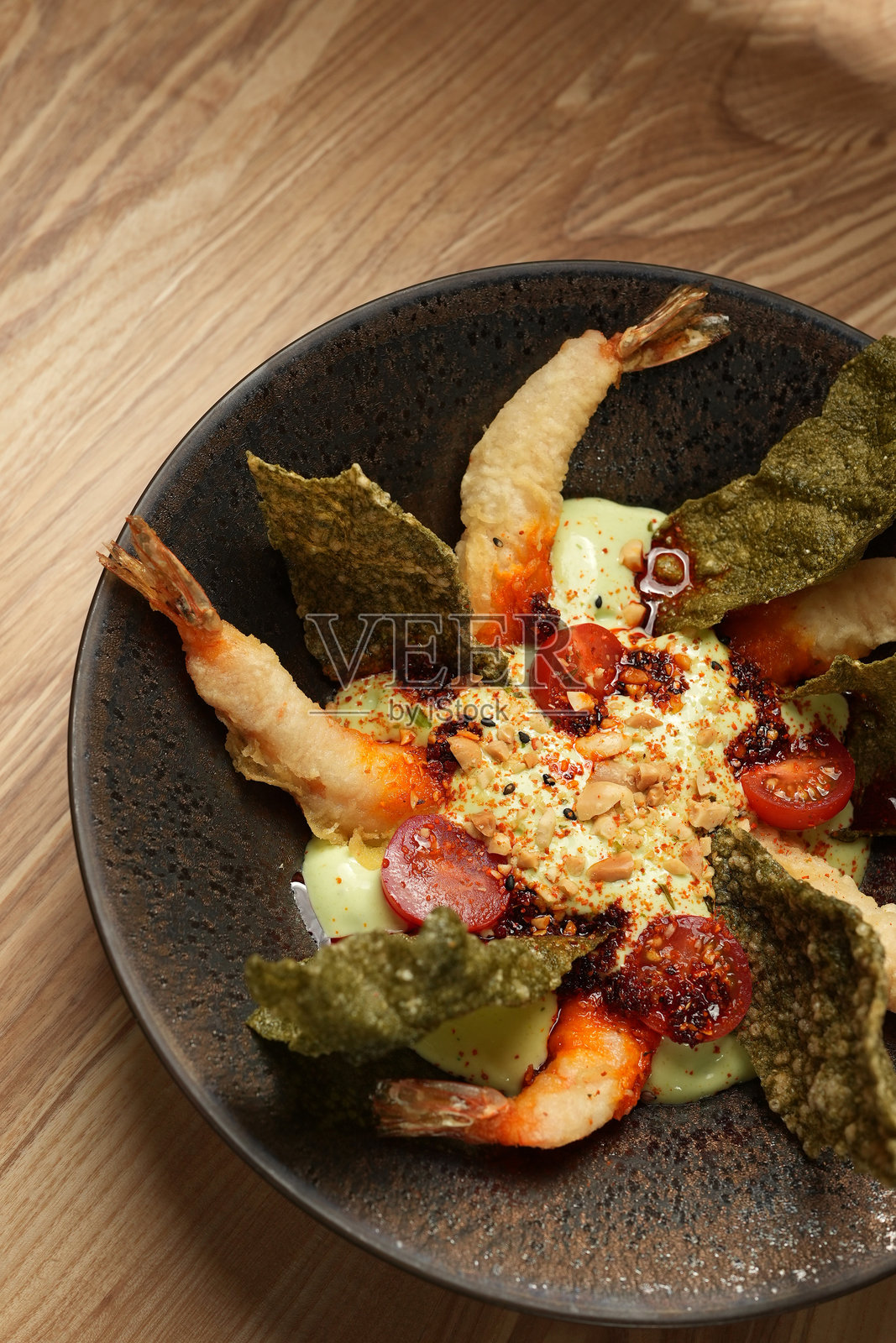 美味的天妇罗虾配鳄梨奶油、脆海苔和樱桃番茄，摆放在深色盘子上照片摄影图片