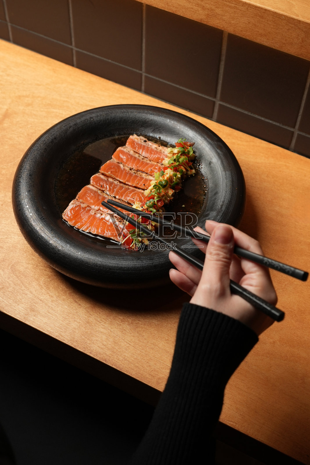 特写镜头：一只手用筷子夹起一片三文鱼刺身，来自一盘精致的亚洲美食。照片摄影图片