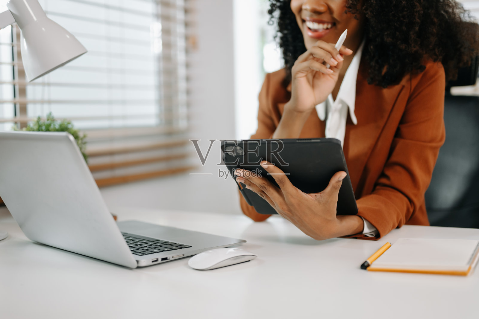 年轻漂亮的女性坐在白色工作桌前，一边用平板电脑一边用笔记本电脑打字。照片摄影图片