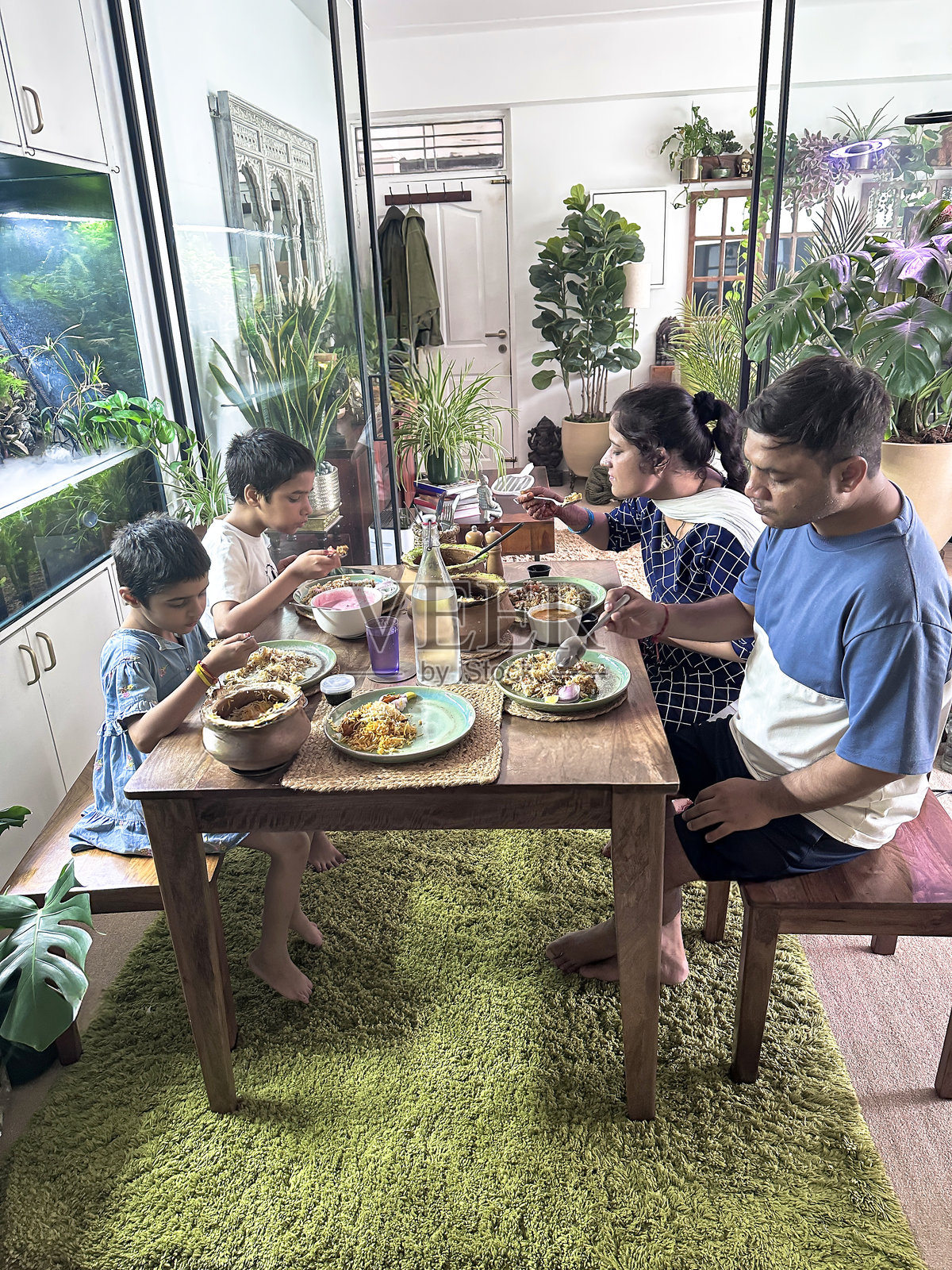 家庭成员和孩子们在餐桌上享用印度外卖晚餐，包含香饭、鸡肉、米饭菜肴、酸奶酱、酸奶和泡菜。照片摄影图片