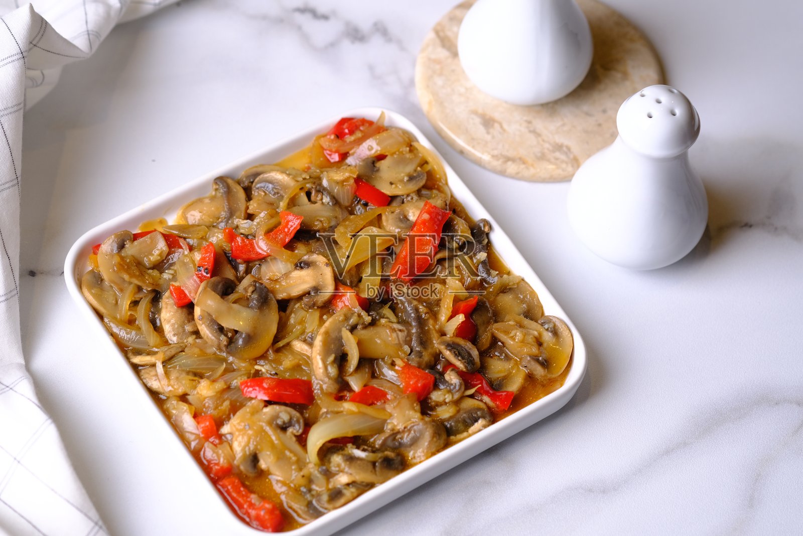 白色陶瓷盘中盛放着香菇、洋葱和红椒，加入黑胡椒烹饪而成。照片摄影图片