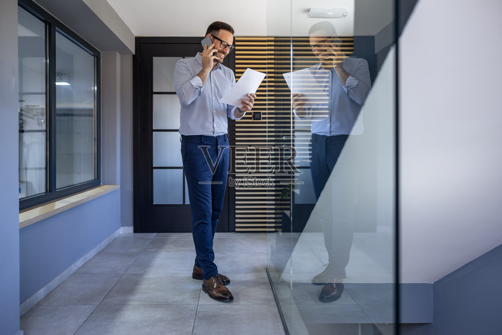 现代办公室中的商务专业人士在明亮的室内空间里一边打电话一边审阅文件照片摄影图片