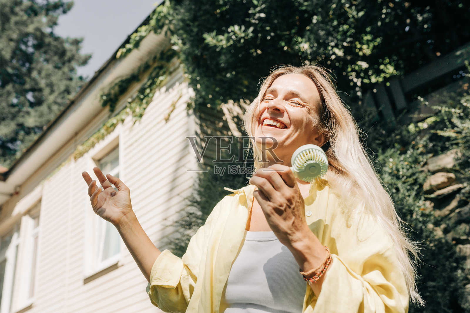 快乐的白人女性在七月的夏天使用便携式风扇。照片摄影图片