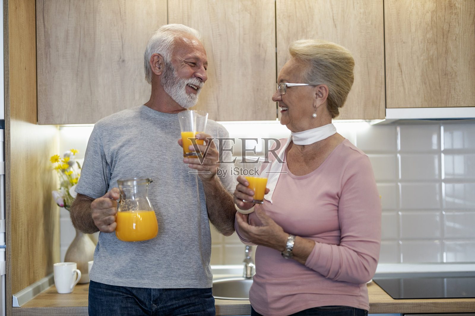一对老年夫妇在阳光明媚的早晨，在现代厨房里一起享用新鲜的橙汁。照片摄影图片
