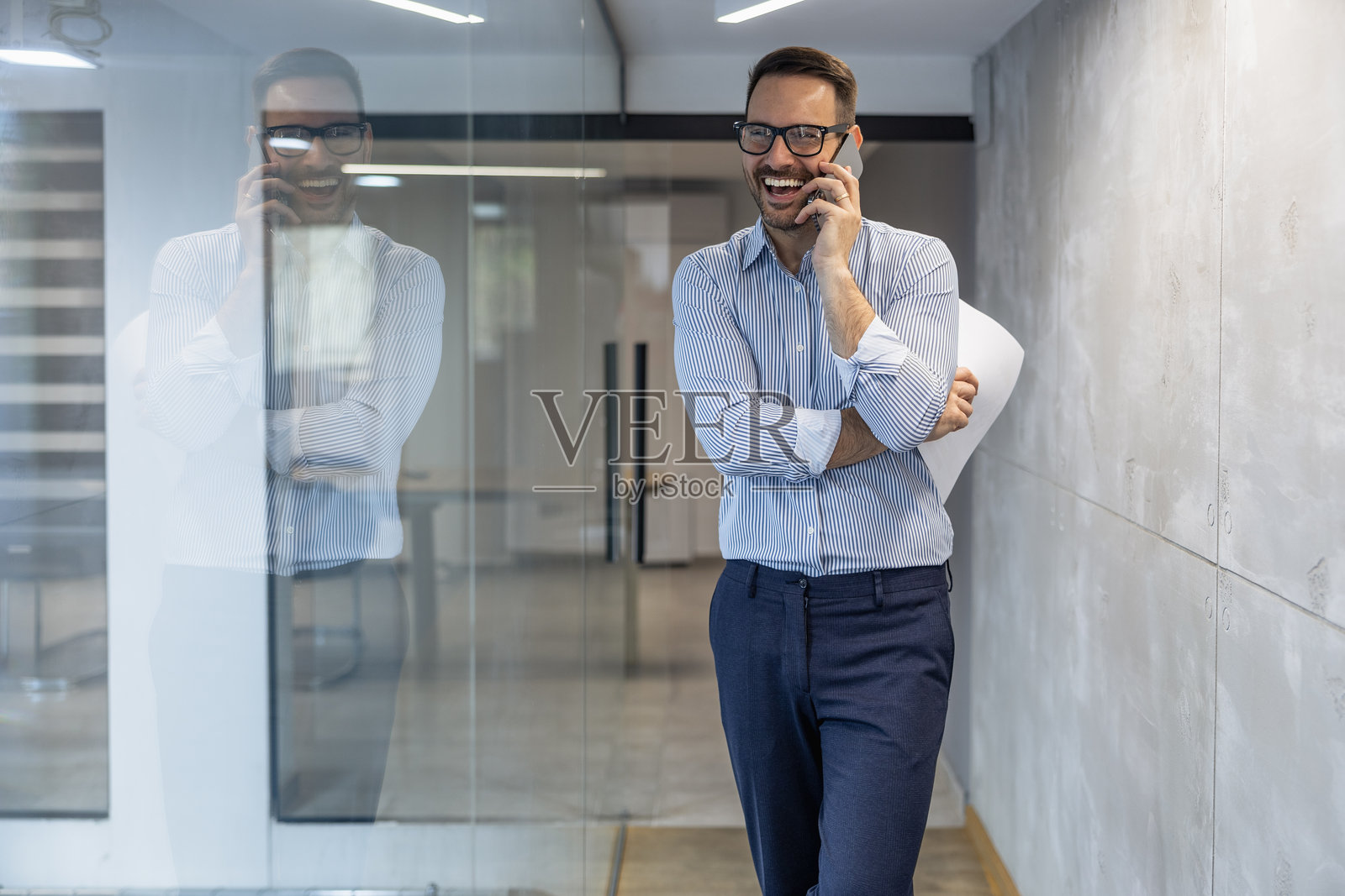 商务专业人士在现代办公室走廊中站着打电话，白天时分。照片摄影图片