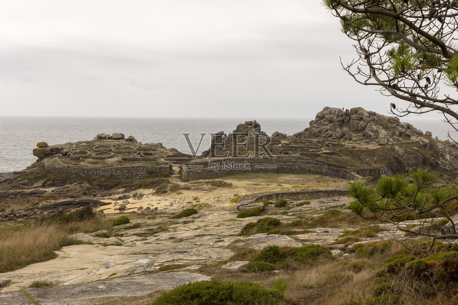 加利西亚巴罗纳的铁器时代防御聚落，位于岩石海滩上，远处有一座小山。照片摄影图片