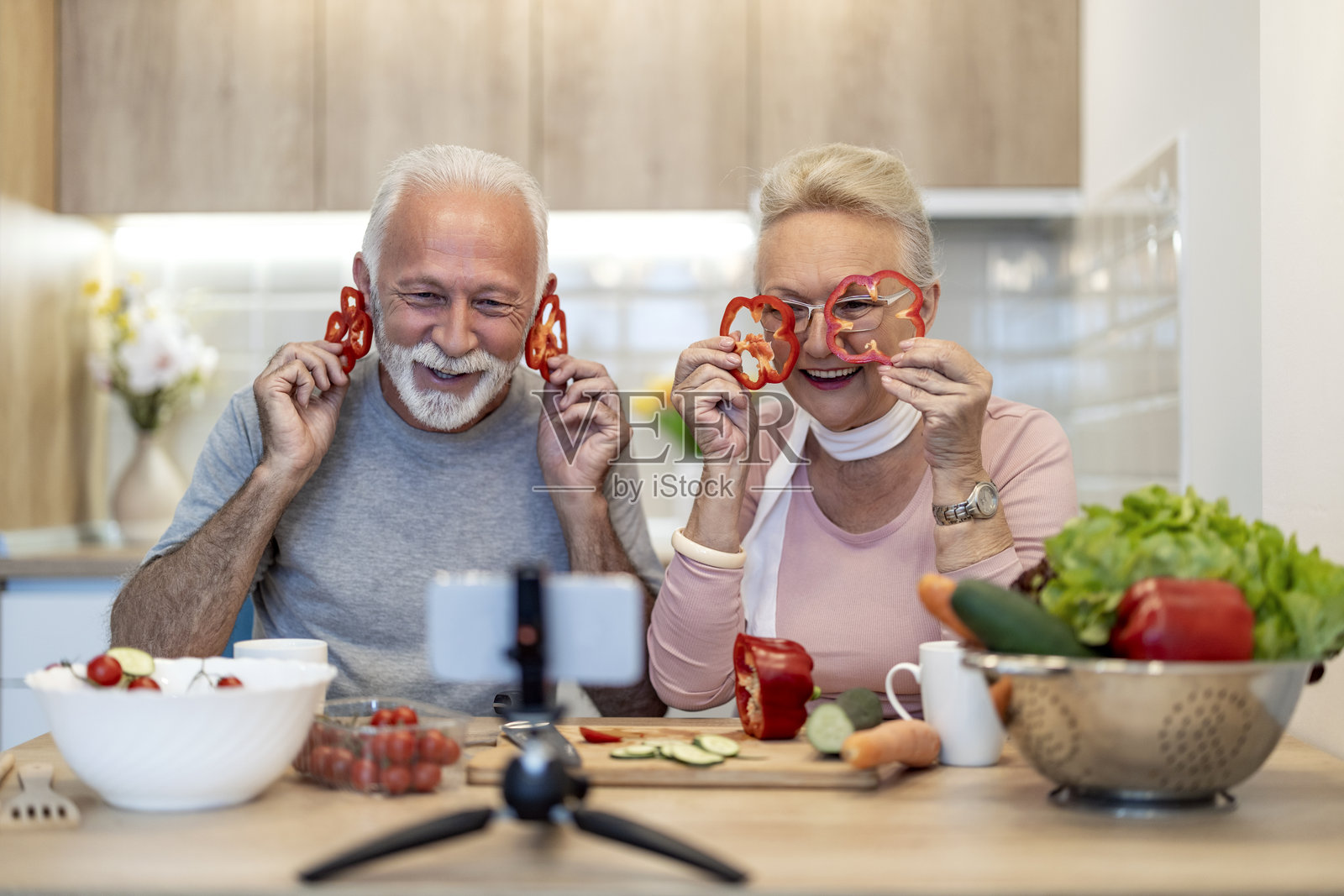 快乐的老年夫妇在明亮的厨房里一起烹饪，享受着与红椒的乐趣照片摄影图片