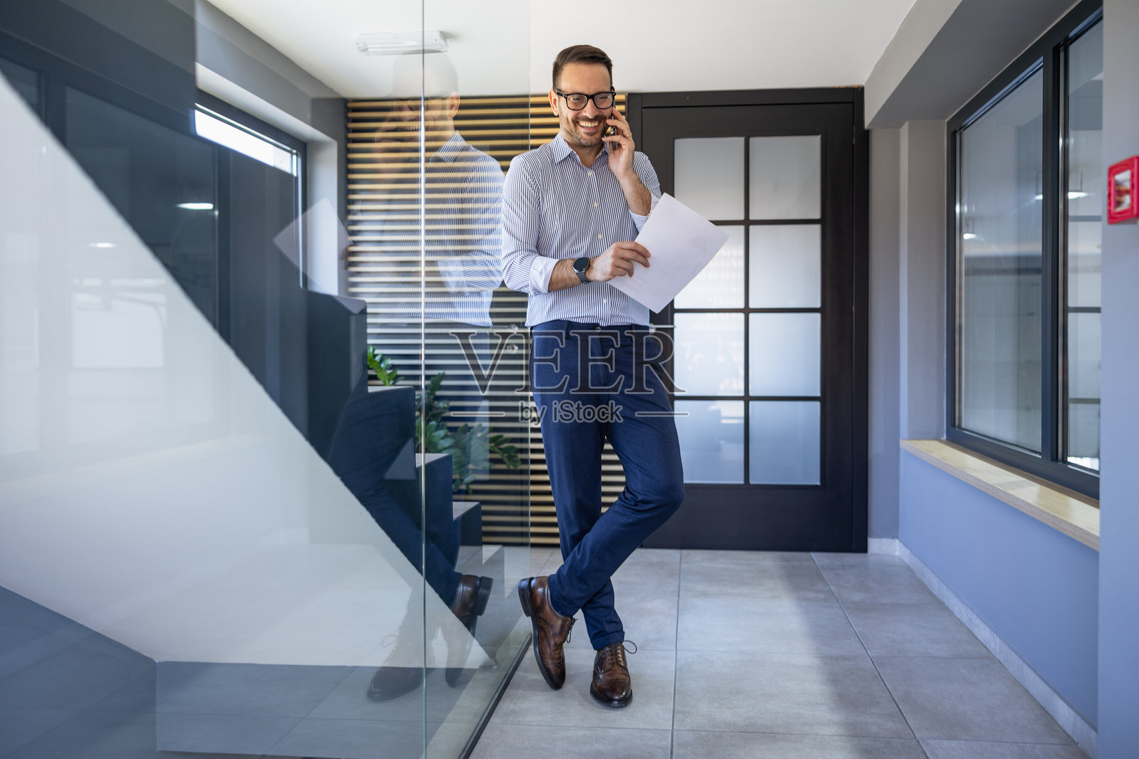 商人在现代办公室环境中工作时，一边打电话一边审阅文件。照片摄影图片