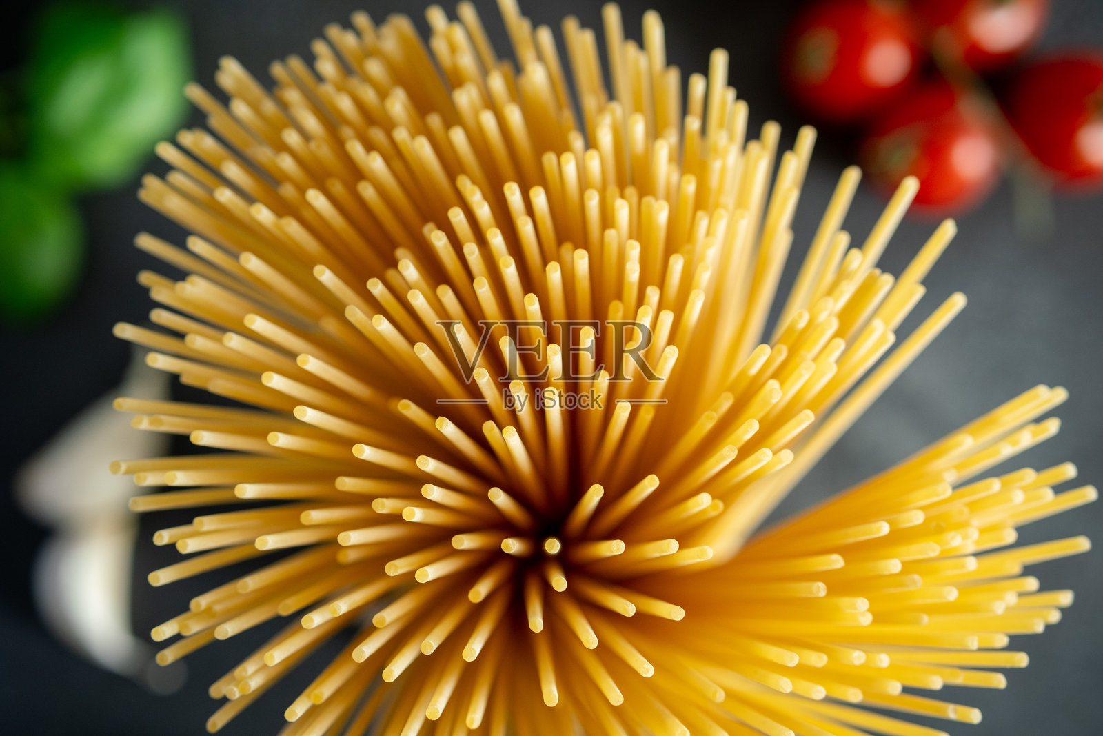 意大利面以圆形束状铺开，背景中有樱桃番茄，象征着地中海美食。照片摄影图片