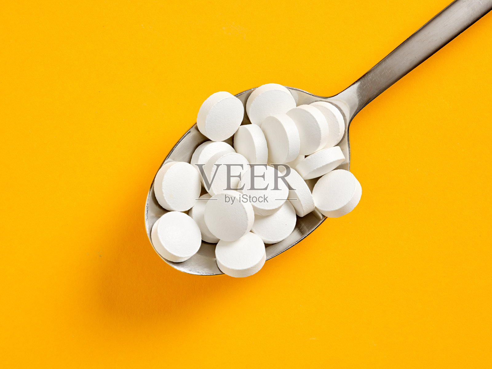 勺子上放着白色药丸，背景为黄色，象征药物过量使用照片摄影图片