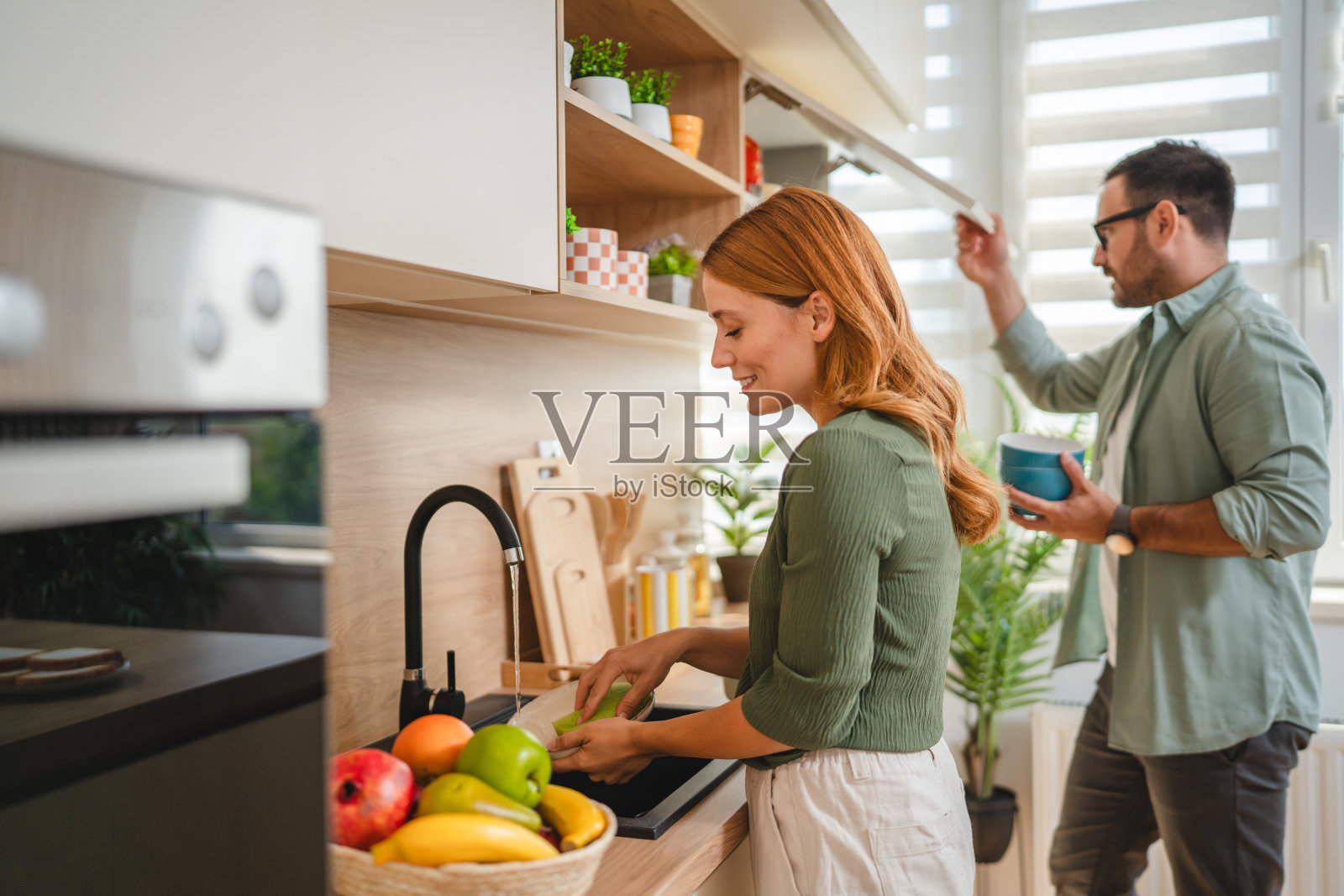 年轻情侣在现代厨房中分担家务，清洗水果照片摄影图片
