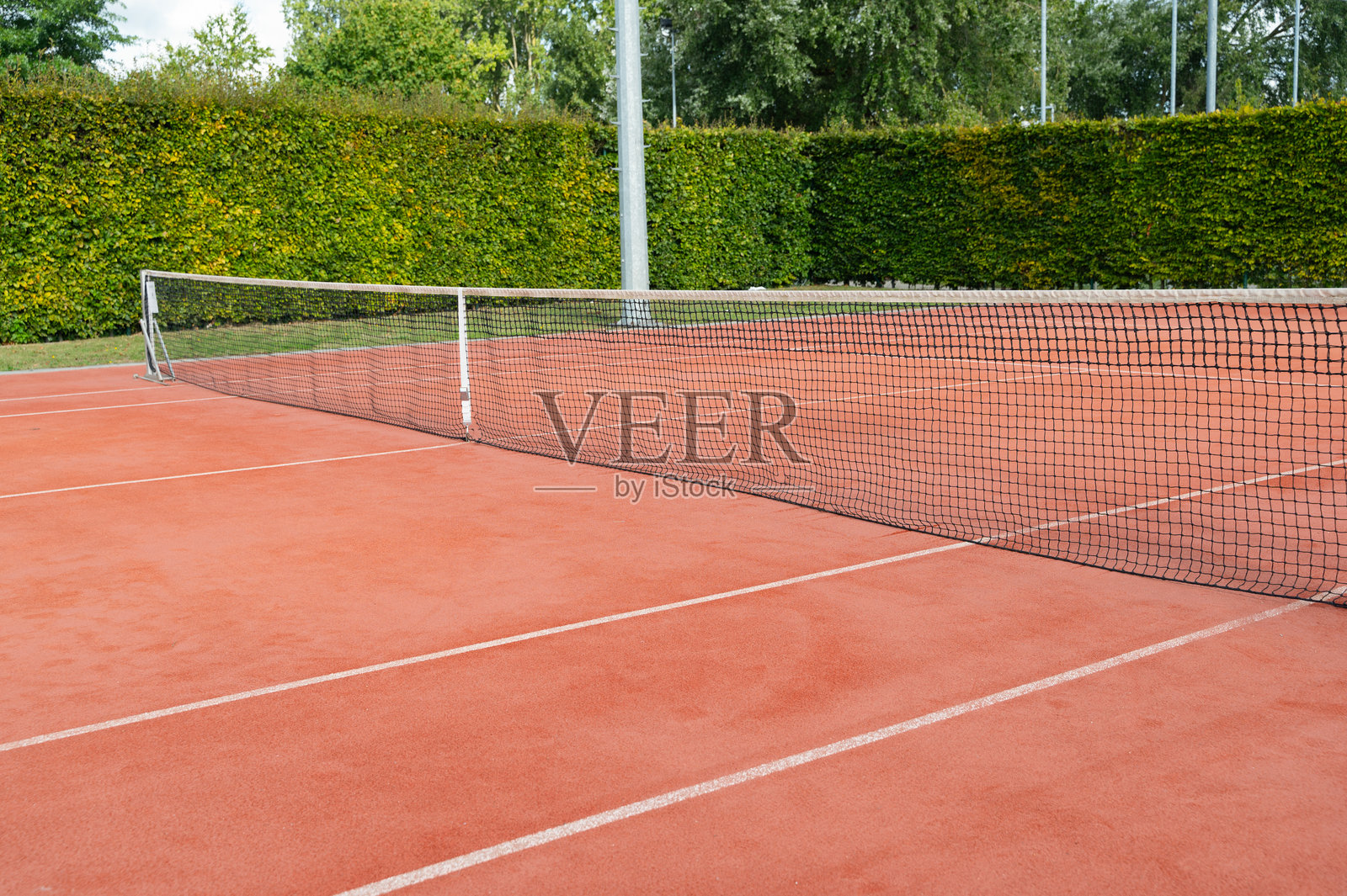 网球场上有一个网，铺有红土，四周环绕着郁郁葱葱的绿植，营造出宜人的氛围。照片摄影图片