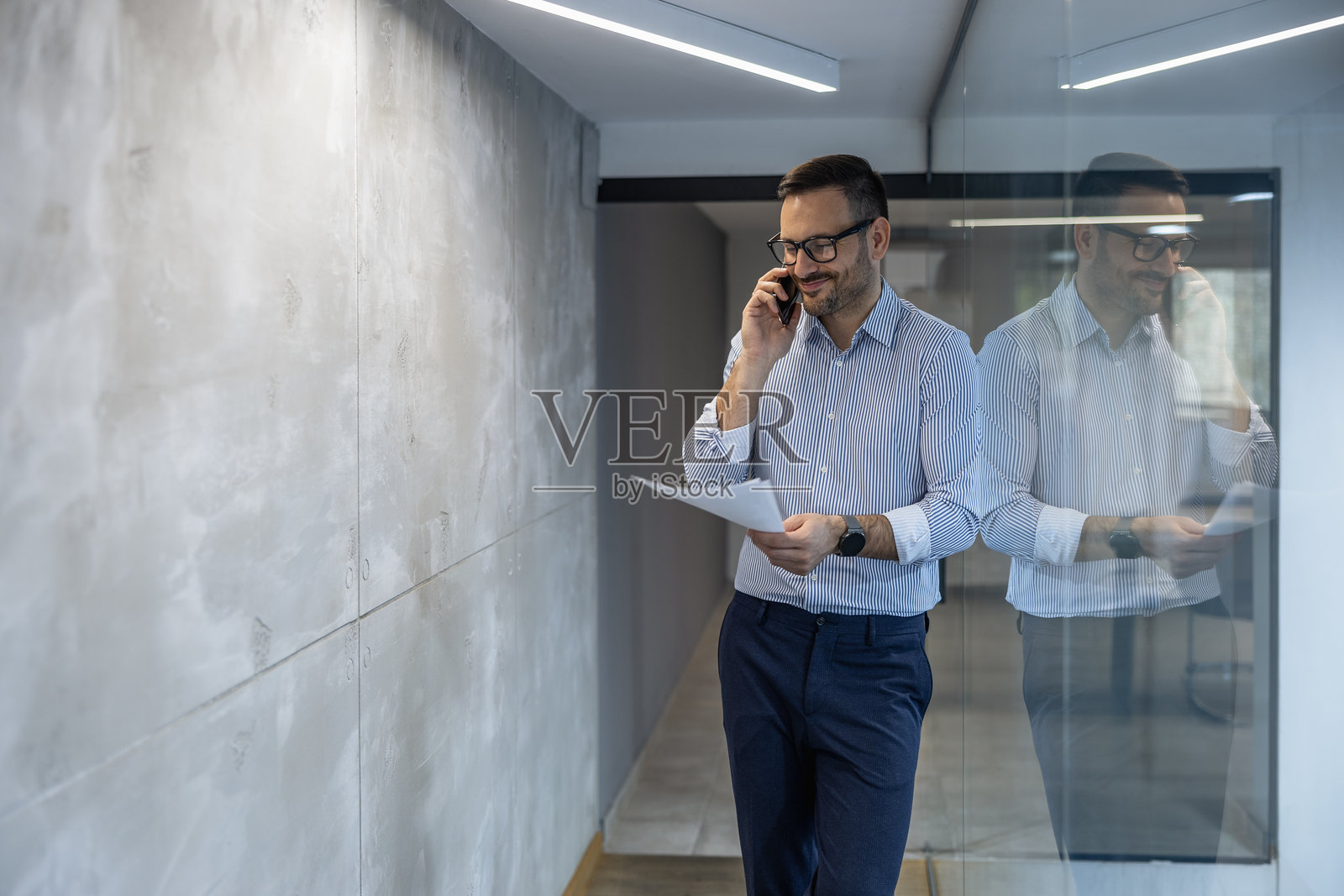 商人在办公室走廊里一边打电话一边查看文件照片摄影图片