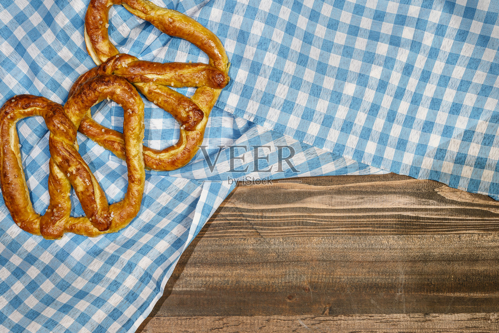 从上方看咸脆饼面包，放在蓝色格子桌布或餐巾上，背景是木桌。留白空间。十月节的概念。巴伐利亚德国文化节的装饰象征。照片摄影图片