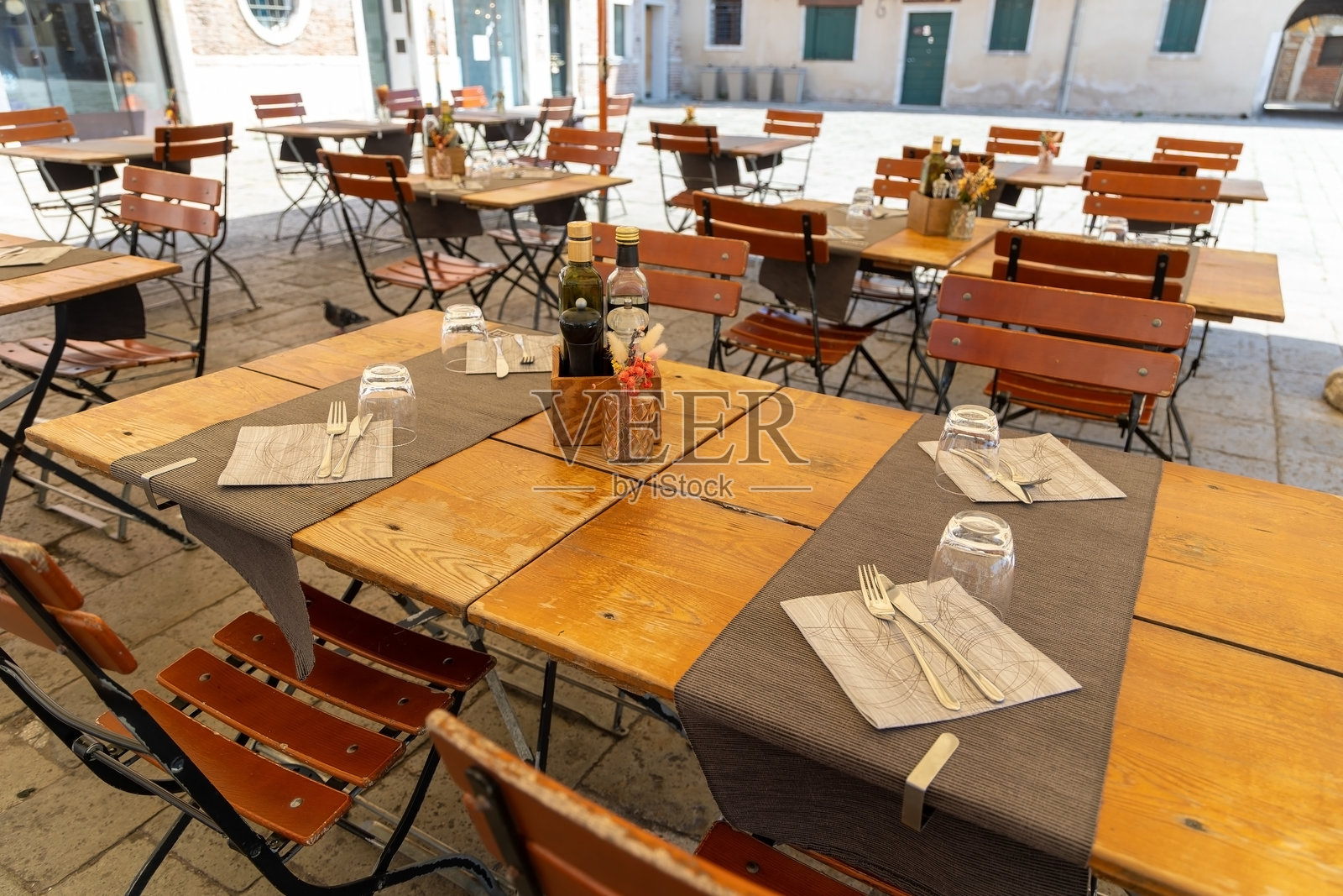 阳光明媚的广场上空荡荡的户外餐厅桌子。安静的欧洲广场上整齐摆放的木桌椅，准备迎接阳光明媚日子里的顾客。照片摄影图片