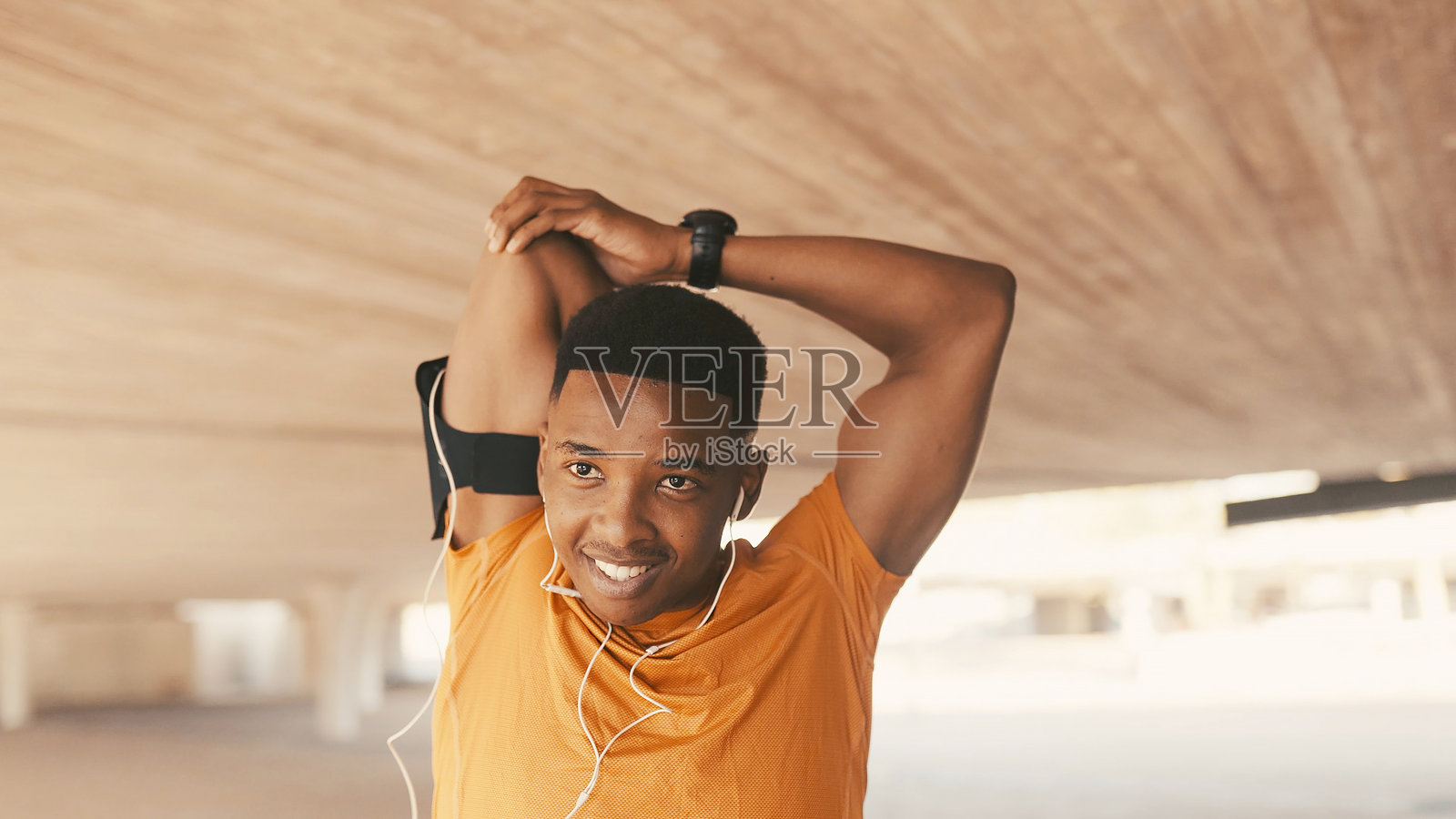 快乐的黑人男性在城市中戴着耳机伸展身体，为健身、锻炼准备或运动做准备。积极的男性正在微笑着热身，准备进行训练或身体活动。照片摄影图片