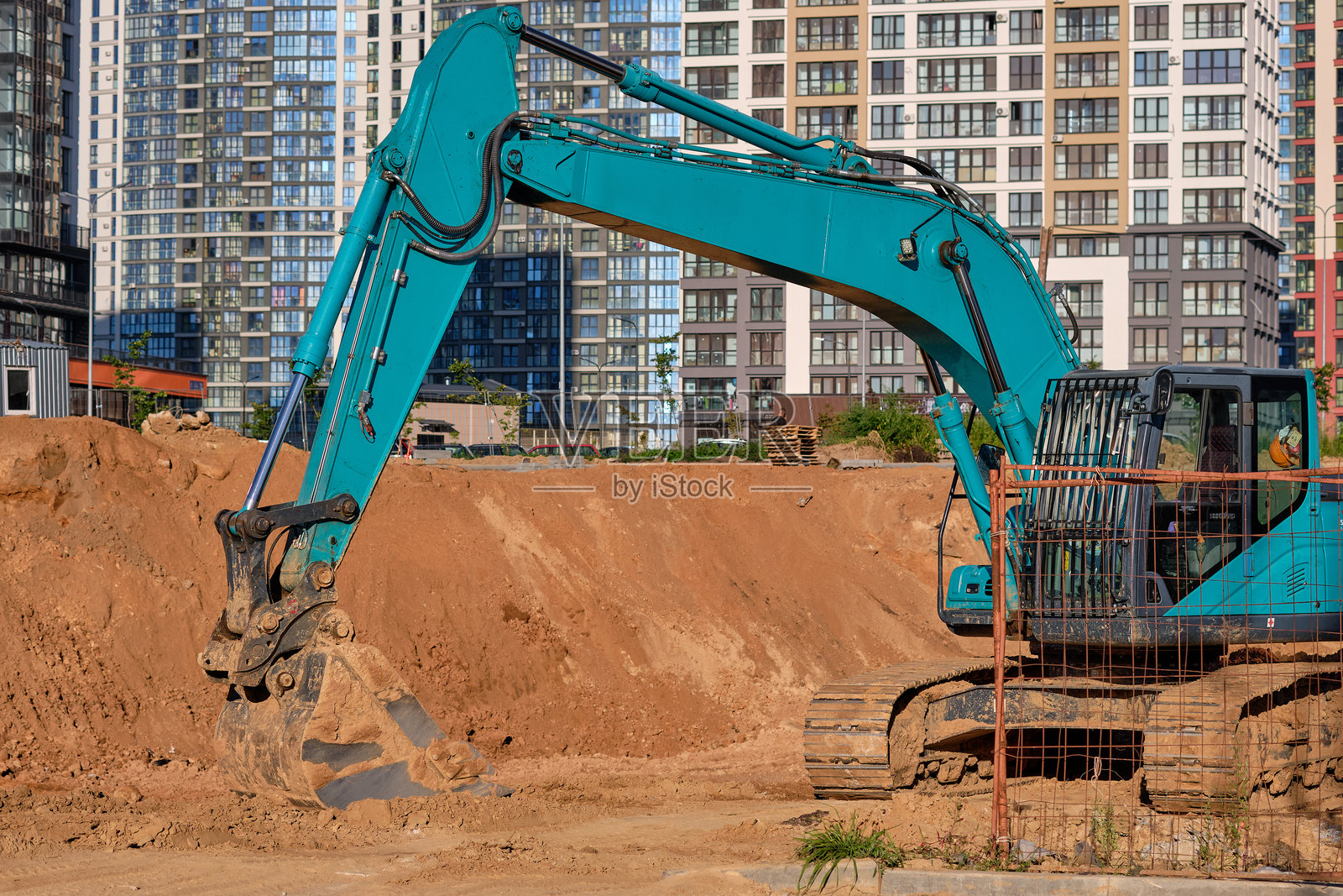重型机械在繁忙的建筑工地上辛勤工作，挖掘土壤并为未来的建筑打下基础，背景是高耸的建筑物。照片摄影图片
