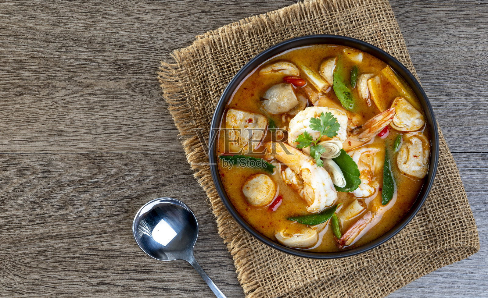 黑碗中的虾汤冬阴功放在木桌上照片摄影图片