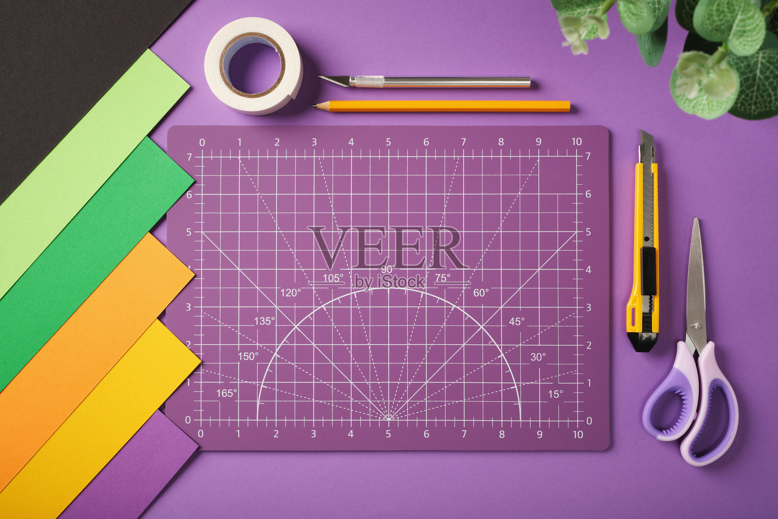 紫色背景上的手工工作空间，配有切割垫、彩色纸张、剪刀、精密刀、胶带和铅笔。留白空间。照片摄影图片