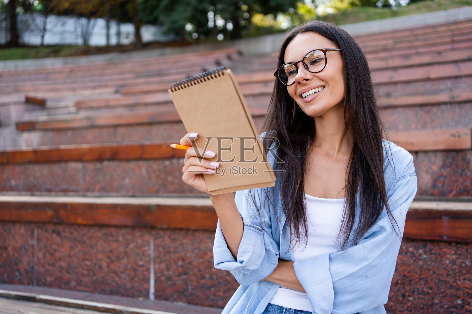 微笑的女性学生教师，戴着眼镜，手中拿着有广告空间的笔记本。大学学习项目，学术教育课程的概念。照片摄影图片