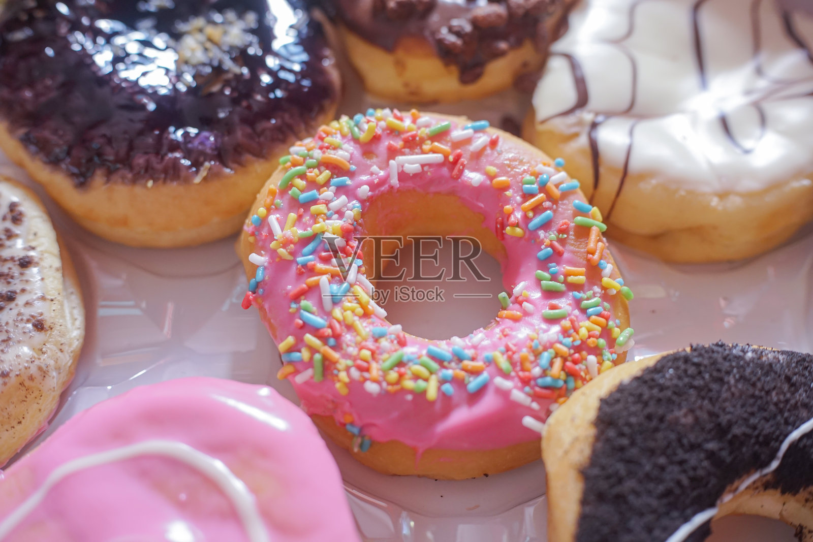 一个人的手从一个装有十二种不同色彩装饰的糕点的盒子里拿出一个美味的甜甜圈。照片摄影图片