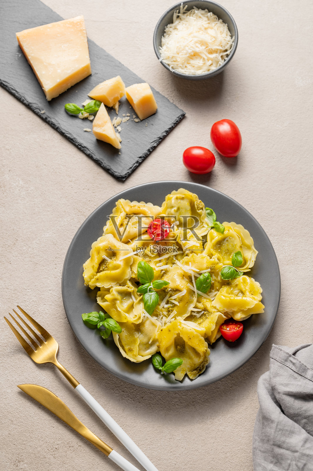 意大利饺子面配帕尔马干酪、香蒜酱和罗勒，摆放在浅色背景的盘子里，旁边有奶酪、西红柿和餐具。照片摄影图片