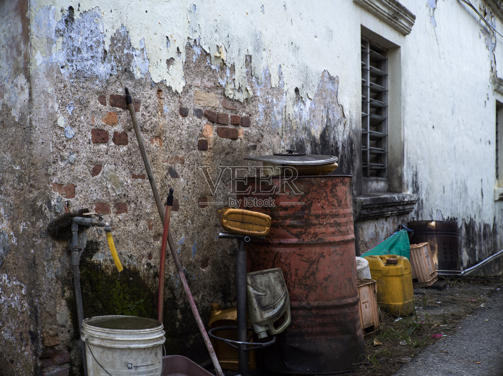生锈的桶和被丢弃的工具靠在风化的墙上照片摄影图片