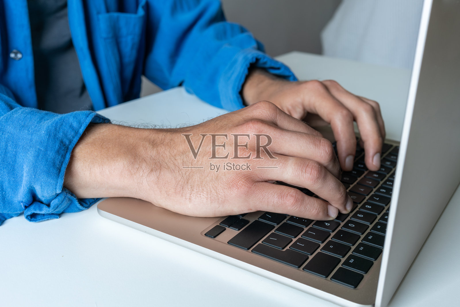 蓝色衬衫的男性手在白色桌子上的笔记本电脑上照片摄影图片